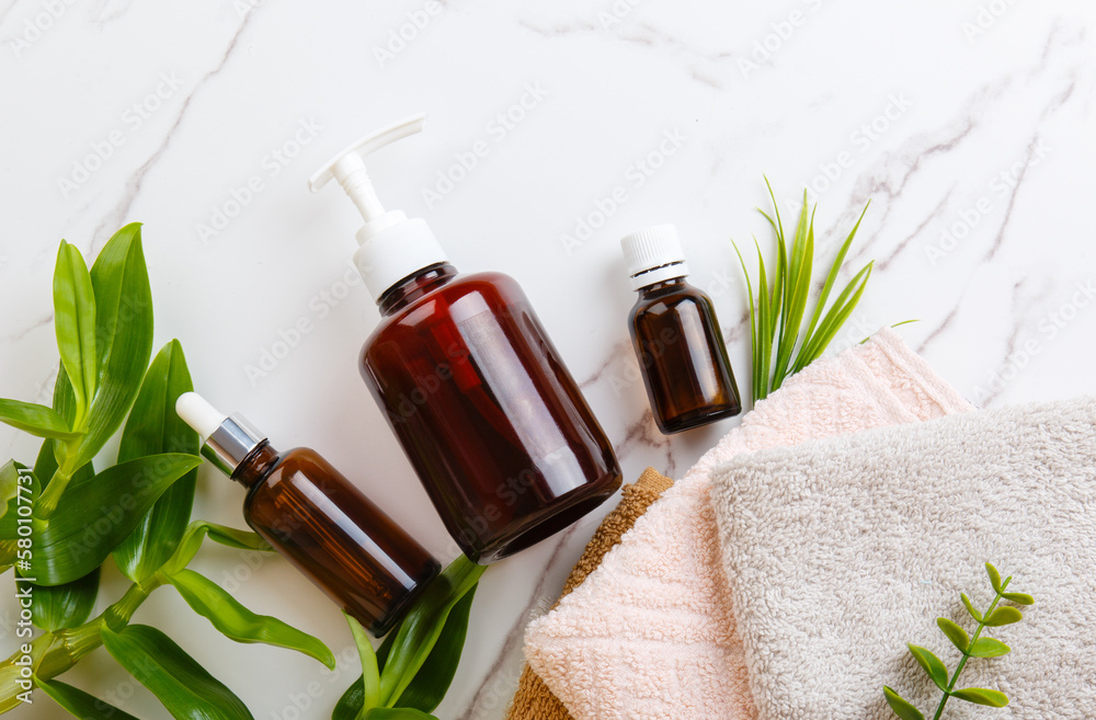 Top view Spa and bath cosmetics on white marble background: serum and face gel, towel rolls, soap. Natural face care products in bathroom. Eco-friendly cosmetics with plants. Natural beauty