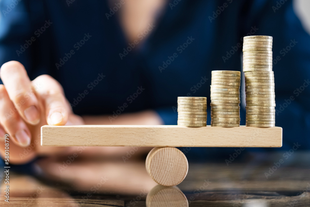 Businessperson Balancing Stacked Coins On Seesaw - obrazy, fototapety, plakaty 