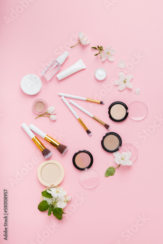 Face care and make up products with spring apple bloom (tonic or lotion, serum, cream, micellar water, cotton pads and makeup brushes) on pink background. Freshness and face care. Decorative cosmetics photo