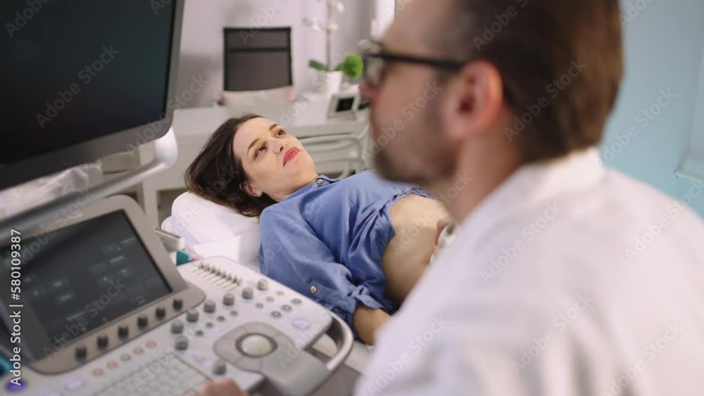 Bearded young professional doctor making ultrasonic investigation to female patient's belly in modern clinic