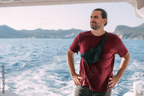 A young, contented man, a tourist rides a boat to the sea, enjoys a sunny day.