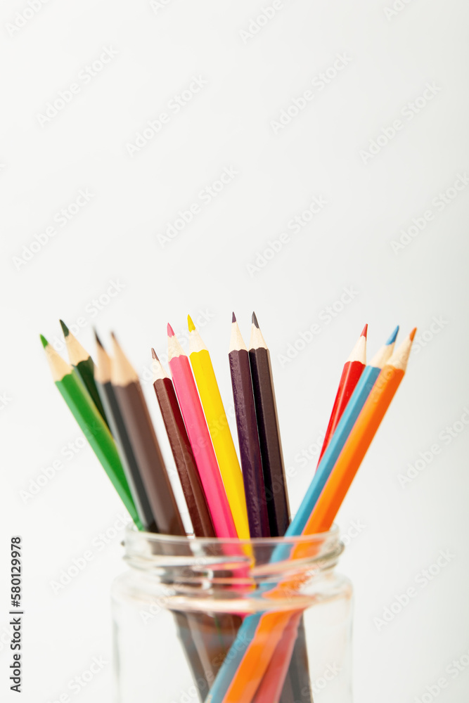 Multi-colored pencils in a glass jar on a white background. Copy space, vertical