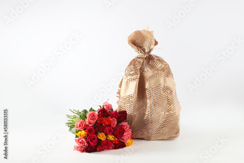 The gift is wrapped in paper. Biodegradable packaging. A bouquet of roses next to the gift. Delivery concept. White background. Isolated object. Copy space.