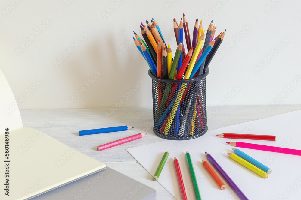Pencil holder with colored pencils and sketch pads on rustic table. Copy space
