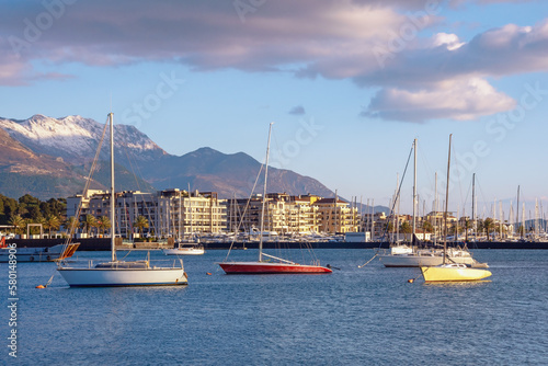 Winter Mediterranean landscape. Montenegro, Adriatic Sea. View of Bay of Kotor, snowcapped Lovcen mountain and Tivat city. Sailboats on water