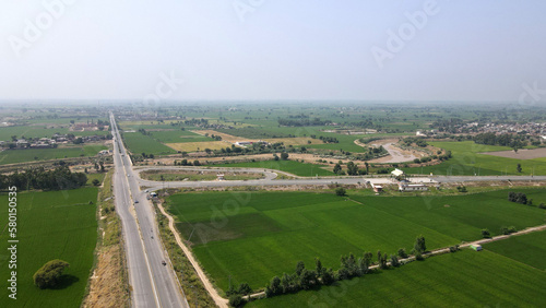An aerial view of Lahore-Sialkot Motorway's Muridkay interchange, capturing vehicles moving on the highway in the vicinity of green rice fields. 
