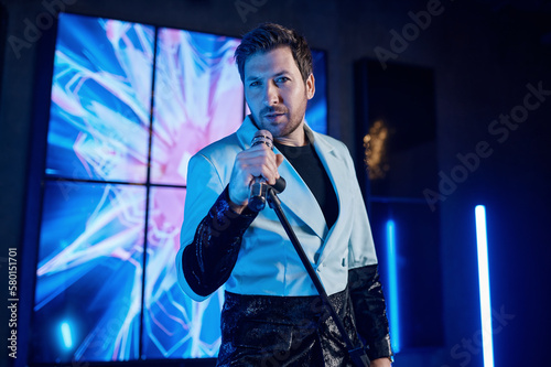 Portrait of handsome attractive singer singing in microphone on stage
