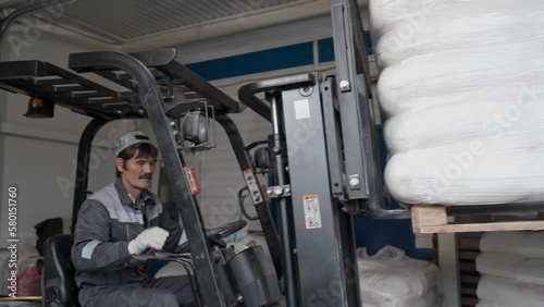 An adult worker in a warehouse unloads pallets with bags of flour on an electric forklift.