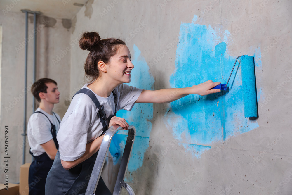 Couple in new home during repair works painting wall together. Happy