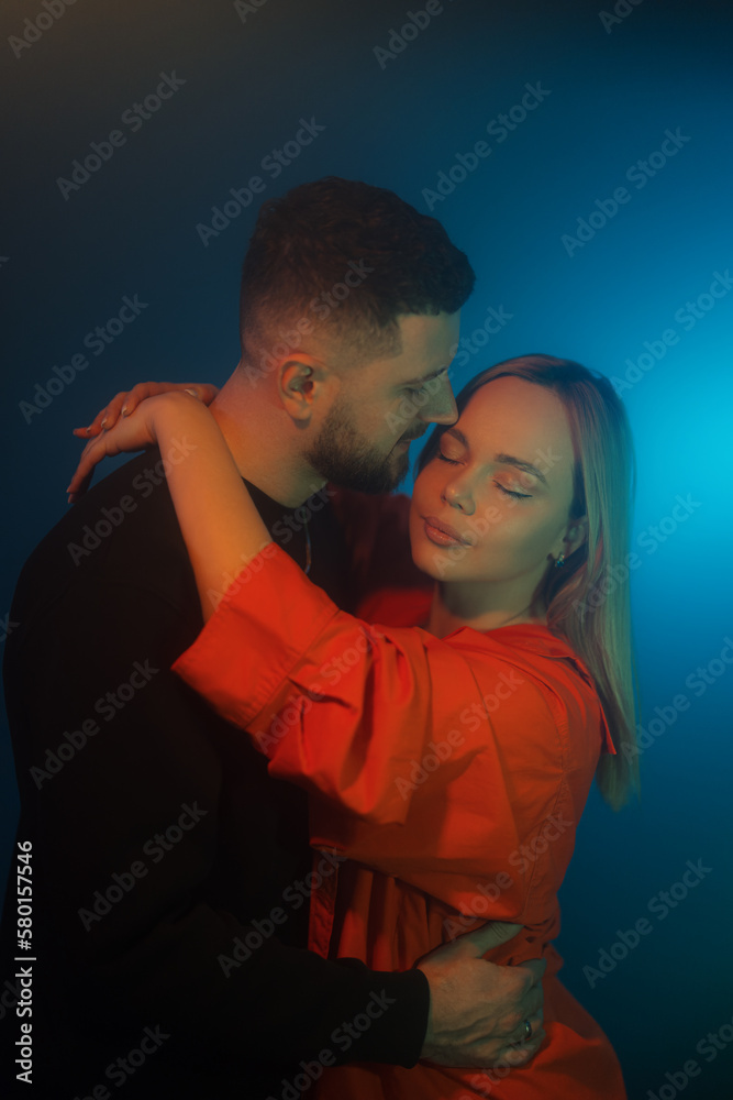 Side view of young man and woman in casual clothes touching each other while standing in dark room with blue neon illumination Side view of young man and woman in casual clothes touching each other while standing in dark room with blue neon illumination