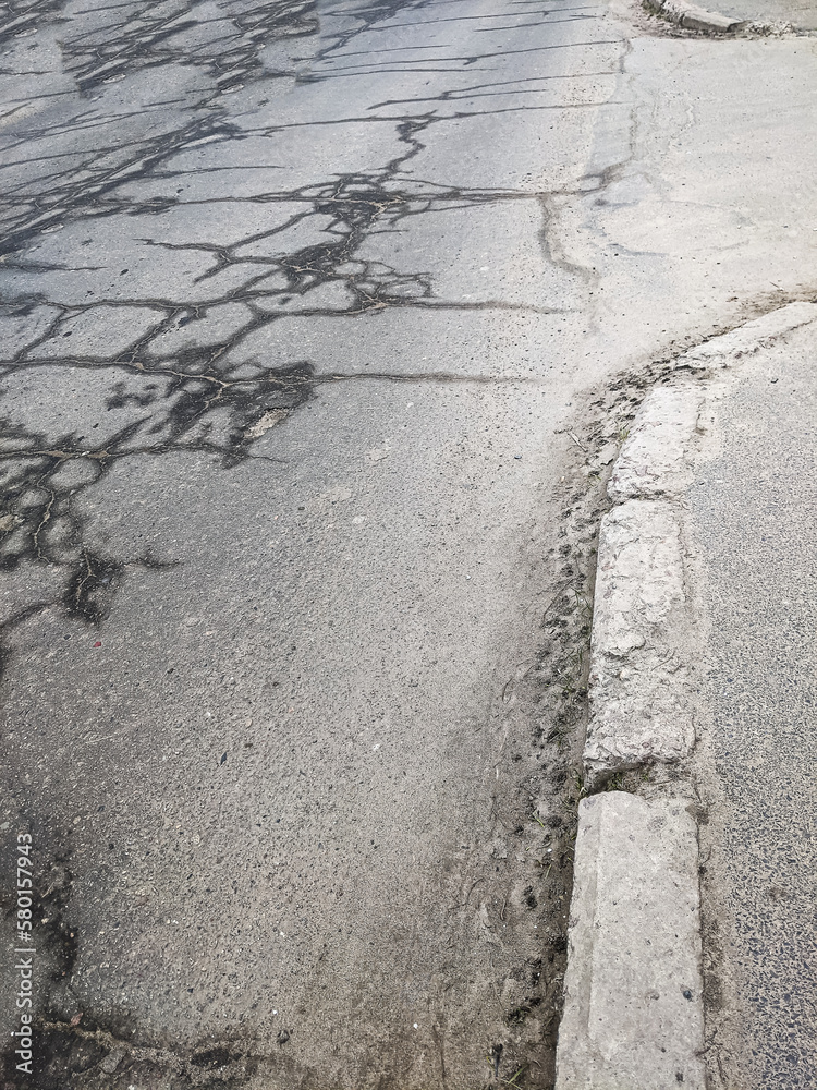 Obraz premium wet cracks on the asphalt surface of the road, a broken curb