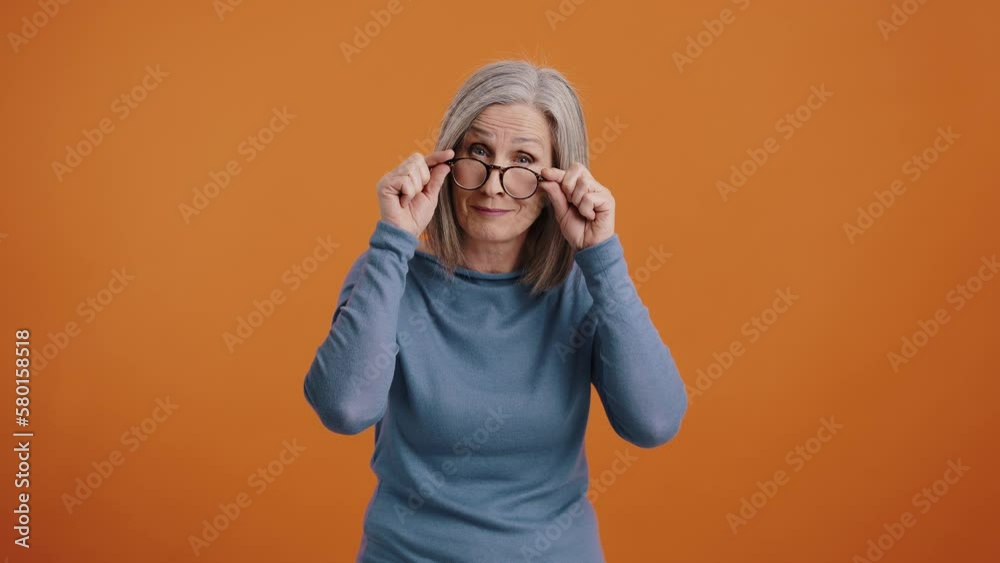 Elderly woman takes closer look lowering glasses and smiles Elderly woman takes closer look lowering glasses and smiles