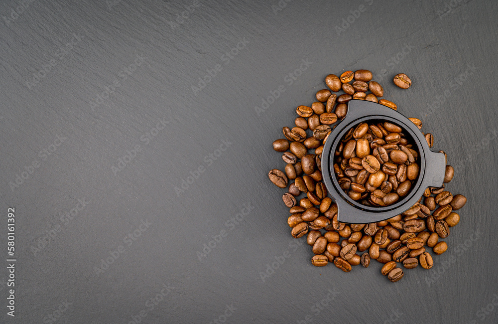 Dosing cup with black matte texture. Top view on black background with coffee beans. Barista tool for dosing coffee beans and using it to when grinding beans.