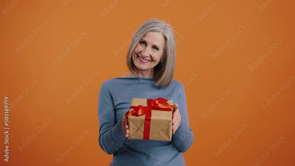 Smiling senior woman presents gift in box with red bow