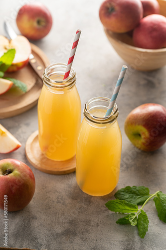 Apple juice glass bottles, with fresh red apples, wooden background. 