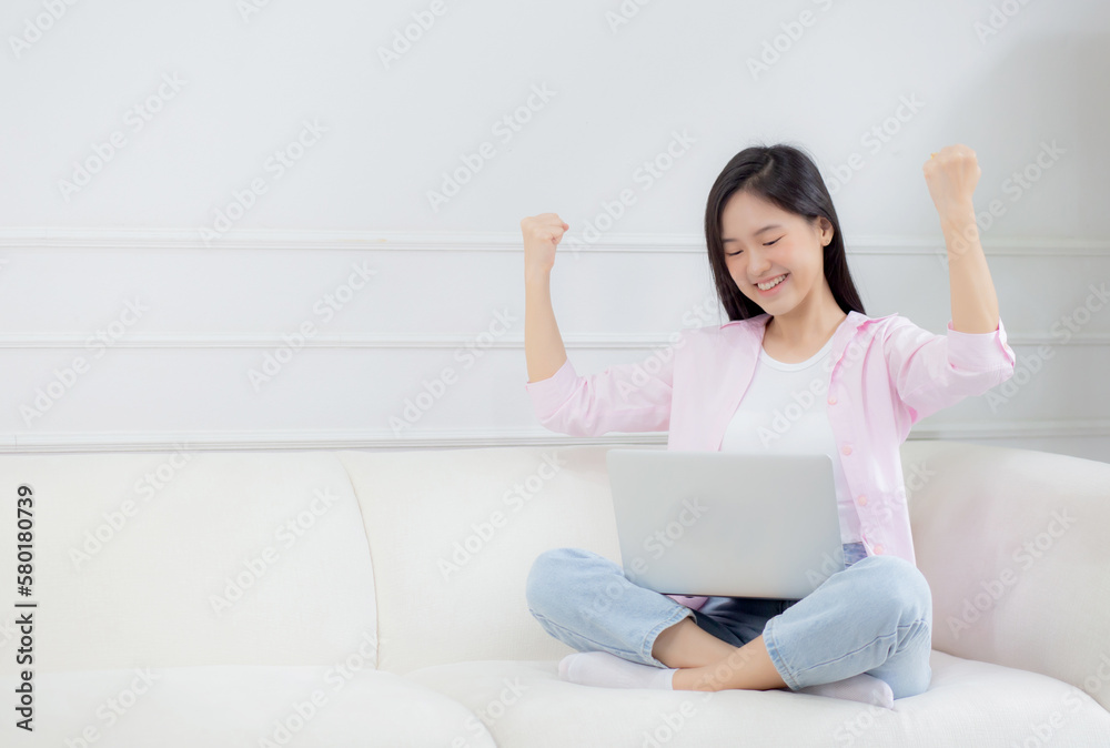 Happiness young asian woman sitting on sofa and working on laptop computer while successful and excitement at home, freelance female using notebook and achievement, business and lifestyles concept. Happiness young asian woman sitting on sofa and working on laptop computer while successful and excitement at home, freelance female using notebook and achievement, business and lifestyles concept.