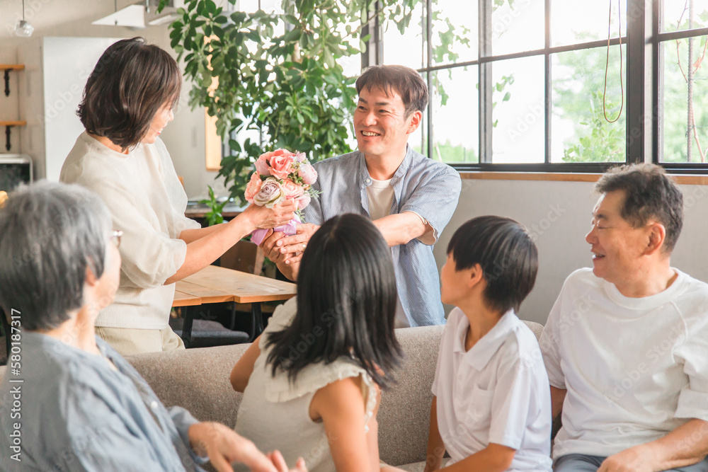 Fototapeta premium 家のソファで家族から花束をもらうママ・母親(三世代家族・ファミリー・家族団欒)