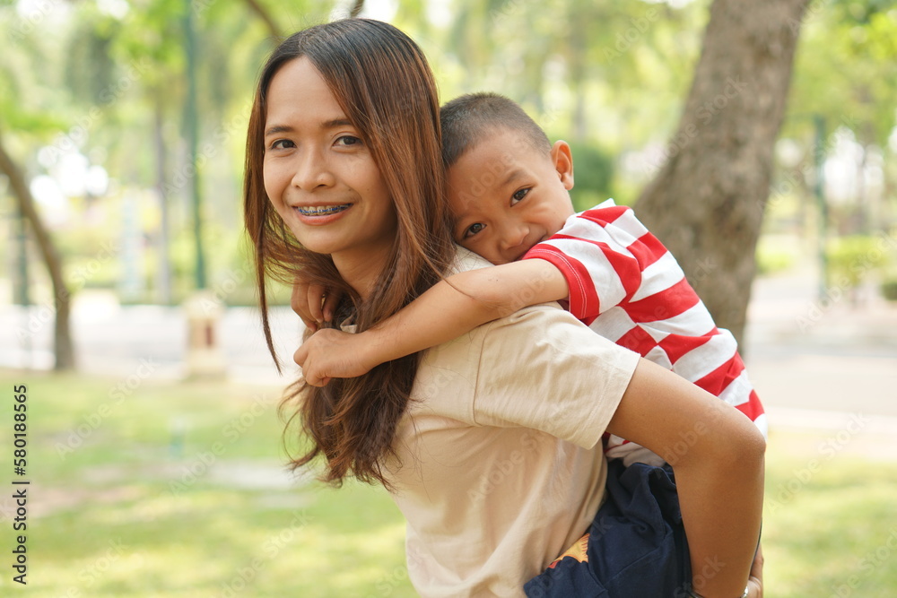 A boy happily rides on his mother's back in the park. A boy happily rides on his mother's back in the park.