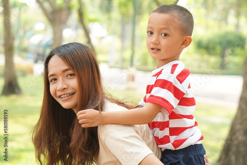 A boy happily rides on his mother's back in the park.