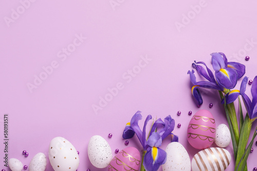Flat lay composition with festively decorated Easter eggs and iris flowers on violet background. Space for text