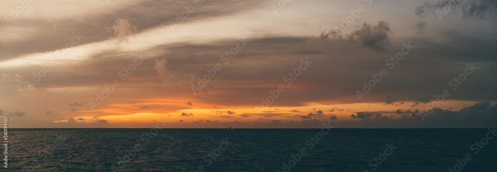 A mesmerizing orange sunset over a serene coastline, backed by a canvas of gray clouds, fading into the tranquil darkness of the night - a breathtaking panoramic view!