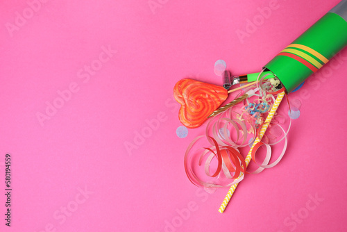 Party cracker and different festive items on bright pink background, flat lay. Space for text