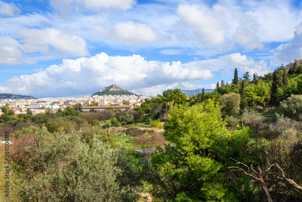 Ruins can be seen among the trees at the ancient Greek Agora at the base of the Acropolis Hill with Mount Lycabettus in view in the distance, in Athens, Greece.
