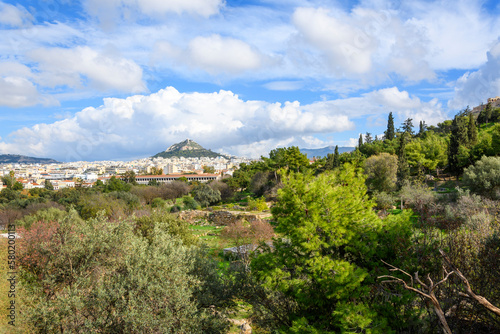 Ruins can be seen among the trees at the ancient Greek Agora at the base of the Acropolis Hill with Mount Lycabettus in view in the distance  in Athens  Greece.