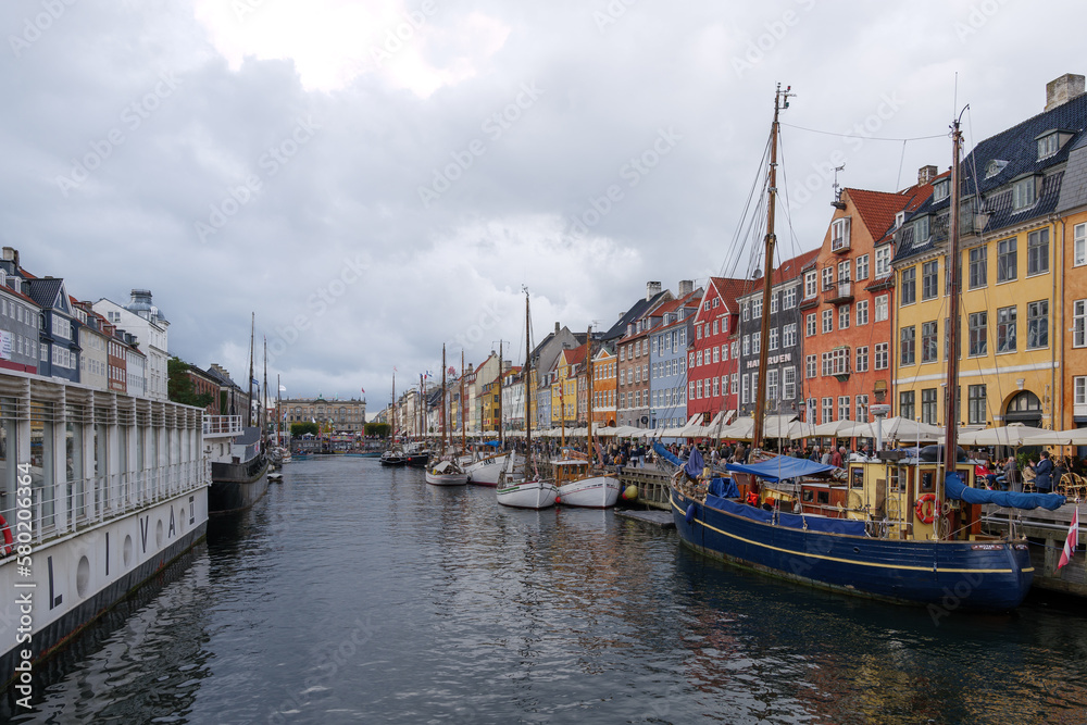 Aerial view of Nyhavn canal with floating tour boat which full of tourists and background of colourful iconic townhouses along waterfront during cloudy day.