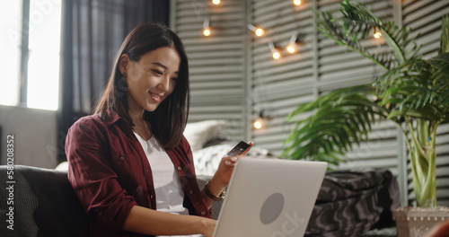 Image of cheerful asian chines woman using laptop while sitting on floor in bedroom. Happy woman doing online shopping at home.  photo