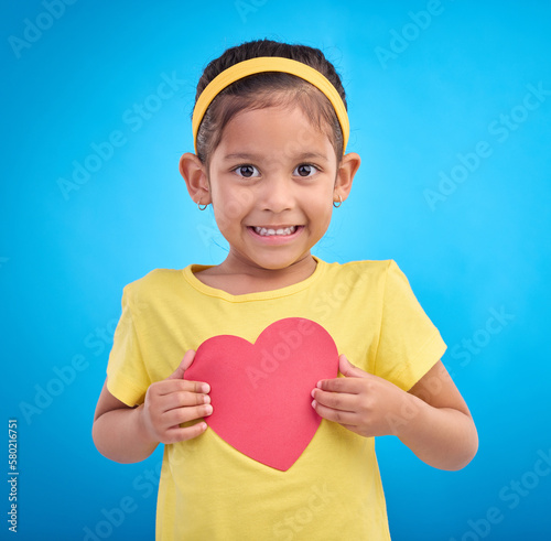 Portrait, smile and girl with heart cutout, joy and cheerful against a blue studio background. Face, Indian female child and kid with love symbol, excited and young person with sign, mockup and happy