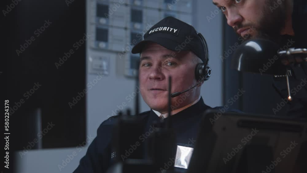 Portrait of security officers look view from security cameras displayed on computer monitors. Man talks with colleague by walkie talkie. Tracking, monitoring and social safety system. CCTV technology.