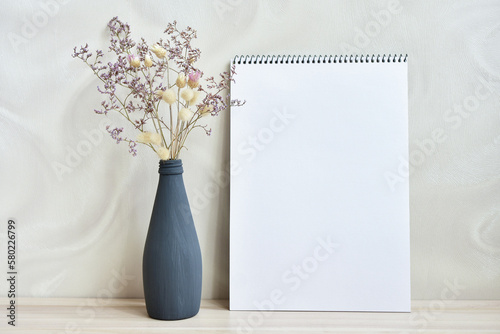 A vase with dried flowers standing on a table near a gray wall with sketchbooks