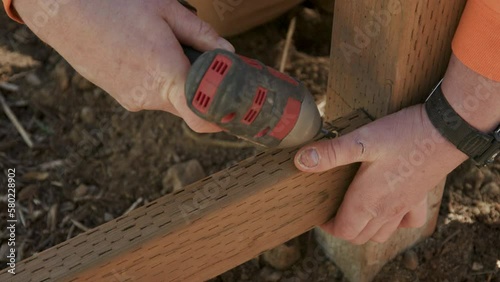 Close Up on Hands of Construction Worker Screwing in Fence Stringer to Post with Power Tool