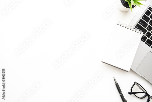 Blank small notebook with pen are on top of white office desk table with laptop computer and office supplies. Top view with copy space, flat lay.