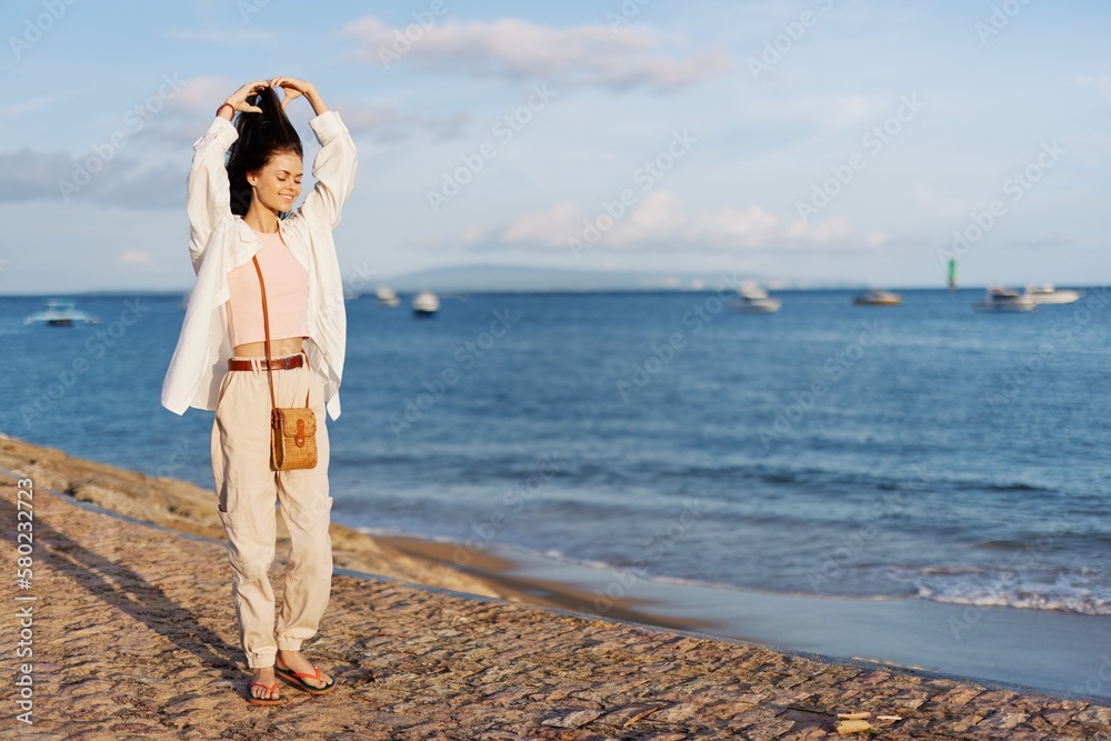 A woman happy with her eyes closed in the sun walking on the beach with her arms spread out against the ocean with a smile, flying hair, tanned skin, relaxation, a trip to the ocean and freedom. A woman happy with her eyes closed in the sun walking on the beach with her arms spread out against the ocean with a smile, flying hair, tanned skin, relaxation, a trip to the ocean and freedom.