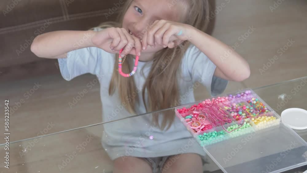 A little girl makes a bracelet out of beads at home