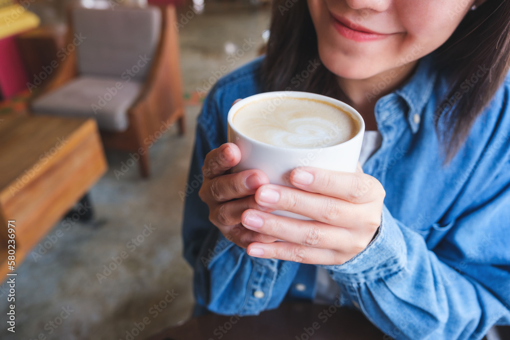 Closeup image of a young woman holding and drinking hot coffee in cafe Closeup image of a young woman holding and drinking hot coffee in cafe