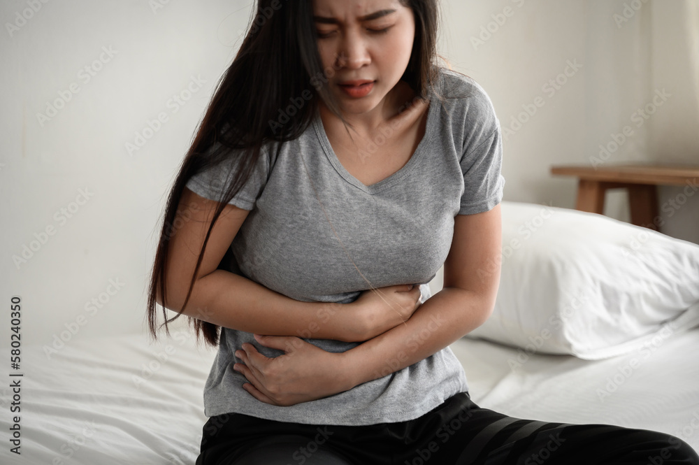 Healthcare medical or daily life concept : Close up stomach of young lady have a stomachache or menstruation pain sitting on a bed. Healthcare medical or daily life concept : Close up stomach of young lady have a stomachache or menstruation pain sitting on a bed.