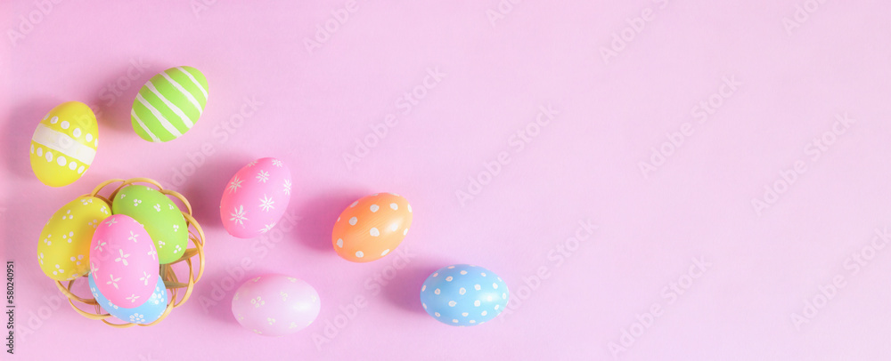 Happy Easter holiday greeting card concept. Colorful Easter Eggs and spring flowers on pastel pink background. Flat lay, top view, copy space.