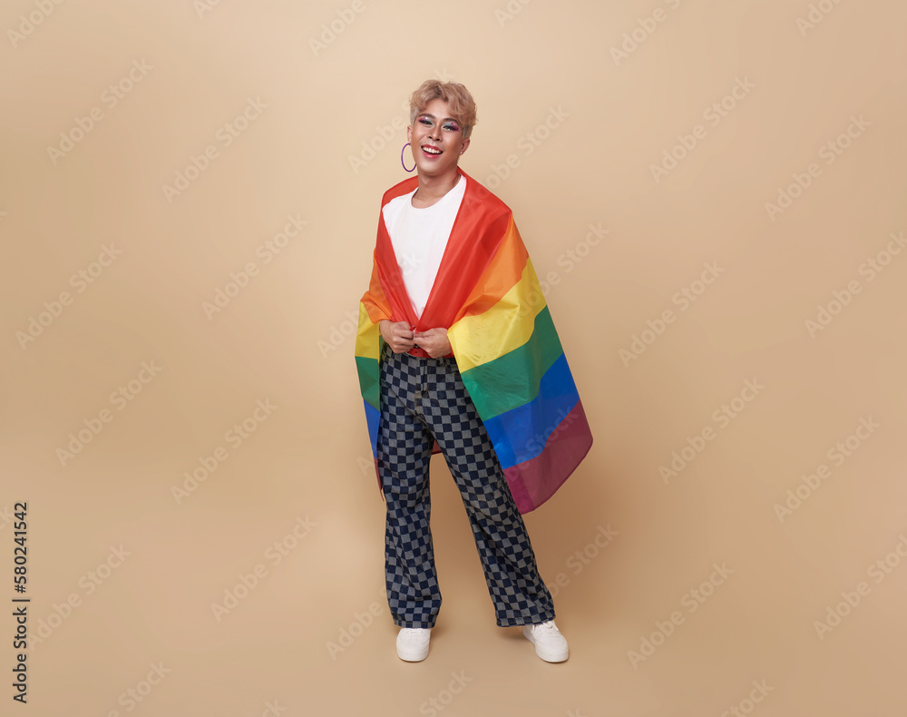 Youth asian transgender LGBT with Rainbow flag on shoulder isolated over nude color background. gender expression pride and equality concept.