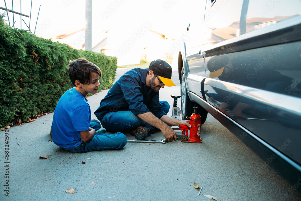 Father teaching son to use car jack while sitting at driveway Father teaching son to use car jack while sitting at driveway