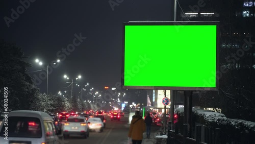 4k Urban view of transport and mockup ad banner in city on dark evening spbas. Vehicles are driving on highway and green billboard standing in modern town in snowy cold weather. Transportation and photo