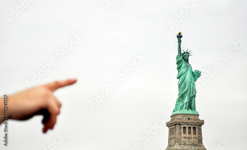 Cropped hand pointing towards Statue Of Liberty against clear sky