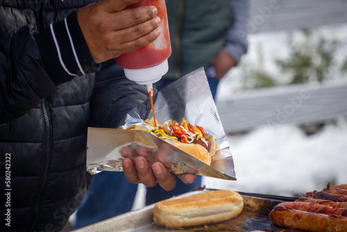 A hot vender putting ketchup on a hotdog