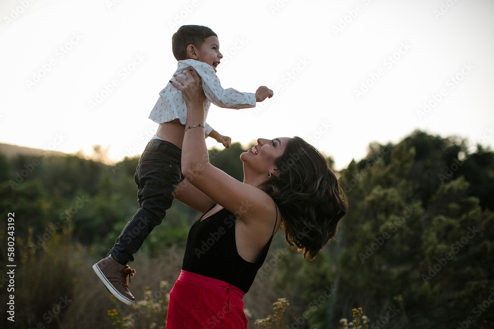 Side view of playful mother lifting son on field Side view of playful mother lifting son on field