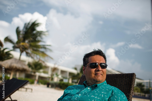 Man wearing sunglasses while resting on lounge chair at beach photo