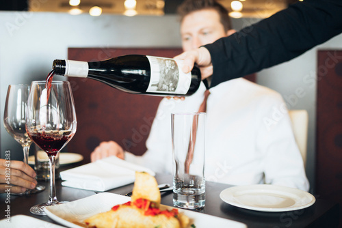 Cropped hand of waiter pouring wine in glass for business people at hotel photo