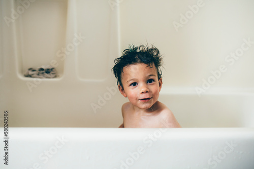 Portrait of shirtless wet boy sitting in bathtub at home photo