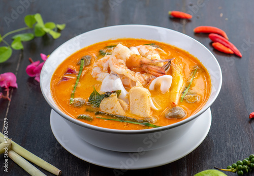 Tom Yam Kung or Tom Yum soup is Thai hot spicy soup shrimp or prawn with lemon grass, lemon, galangal, mushrooms, coconut milk and chili in bowl on wooden table top view, famous Thai food cuisine.